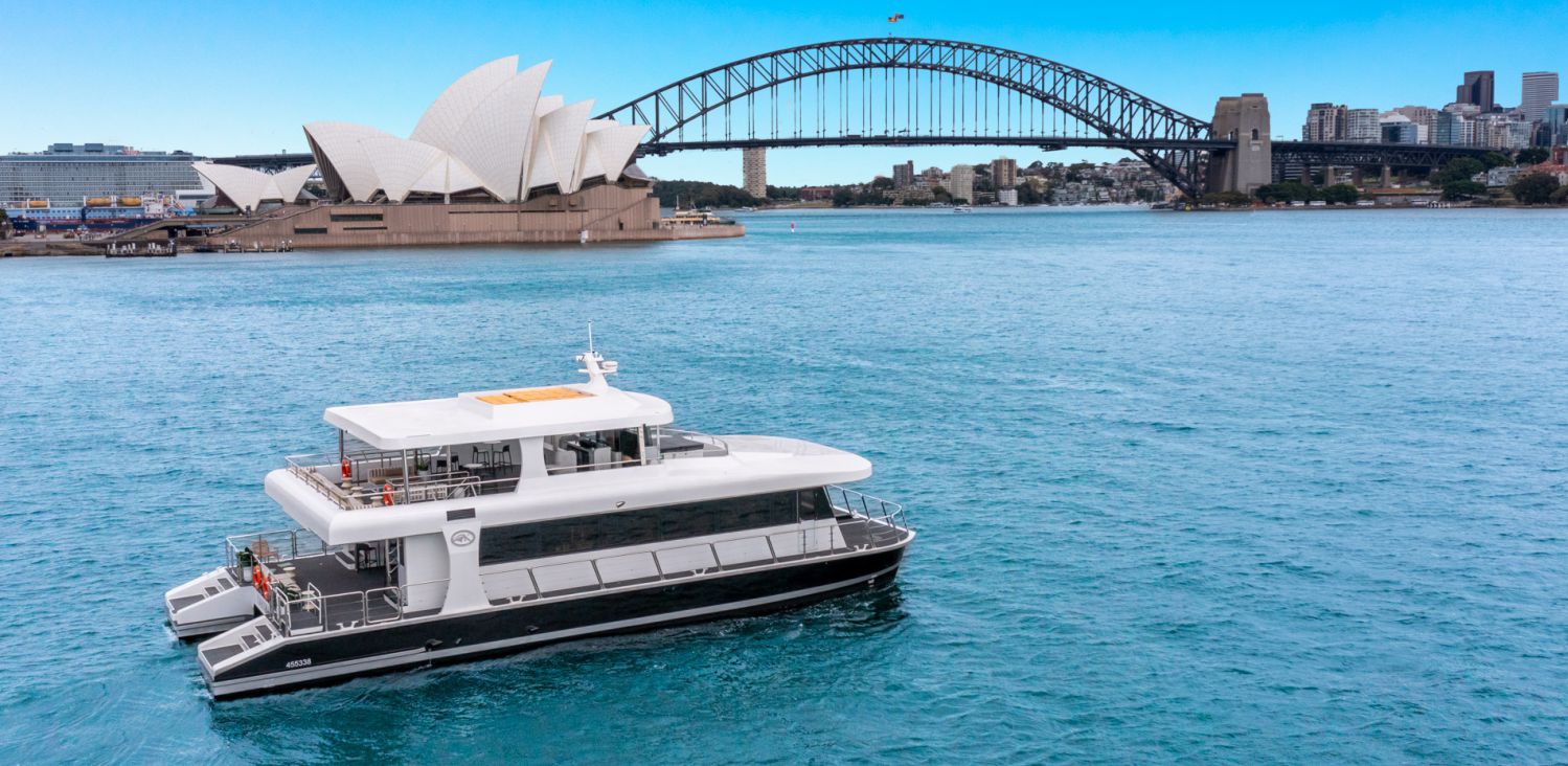 A luxury yacht cruising on a bright day in sydney harbour, with the iconic sydney opera house and harbour bridge in the background.